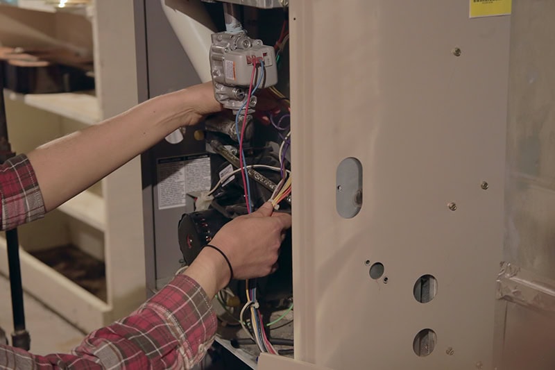 An HVAC technician working on a furnace unit system.